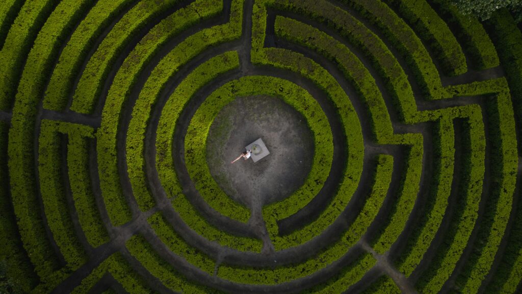 Drone shot of a woman standing in the center of a lush green hedge maze.